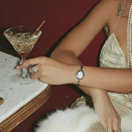 Person in a sparkly dress holding a cocktail glass with a red background