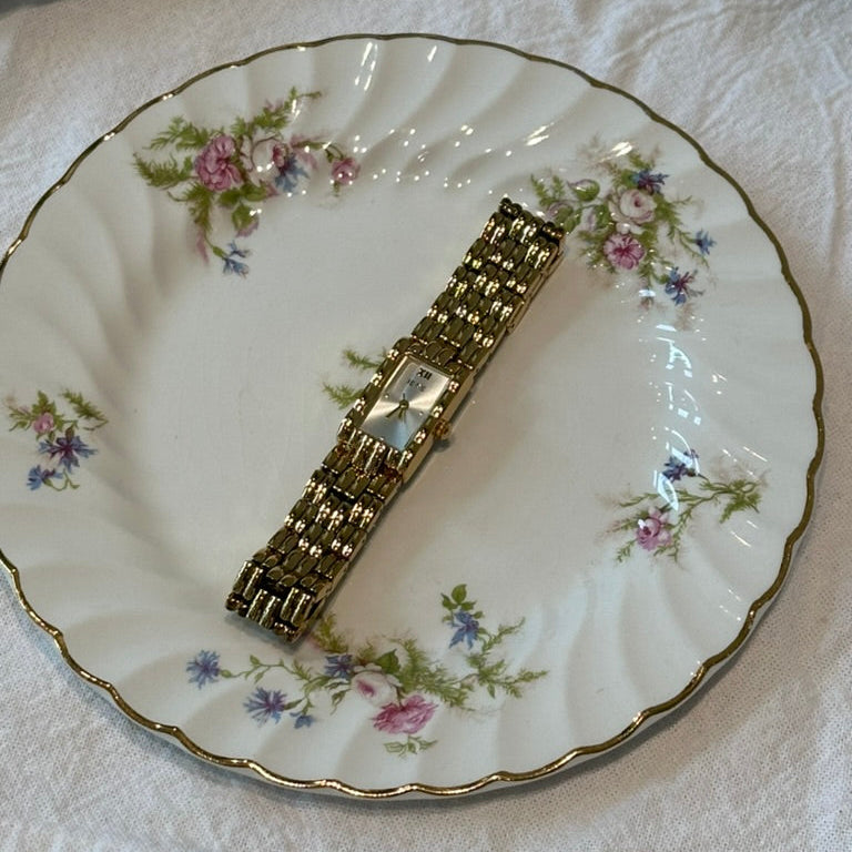 Gold watch on a decorative plate with floral patterns