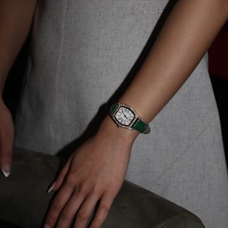 Hand wearing a watch with a green strap against a neutral background