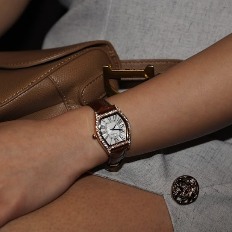 Close-up of a wrist wearing a watch with a brown leather strap, sitting on a gray surface.