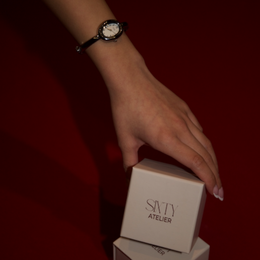Hand holding a small box with 'SIXTY ATelier' branding on a dark background