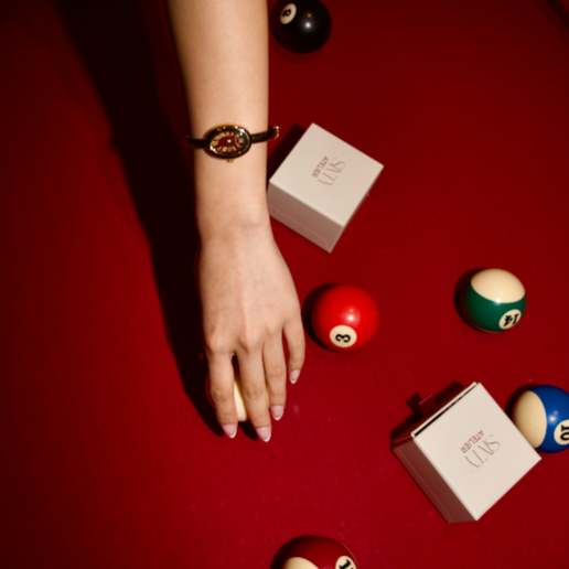 Hand with a bracelet on a red surface with billiard balls and boxes.