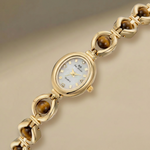 Gold bracelet watch with tiger eye stones on a beige background