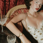 Woman in a vintage setting with drinks and a gold watch
