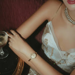 Woman in elegant attire holding a glass of champagne with a focus on jewelry and dress details.