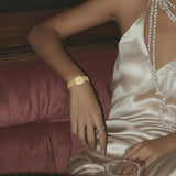 Woman in a satin dress with jewelry sitting on a couch next to a glass of whiskey.