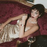 Woman in a gold dress lying on a red velvet couch with a glass of wine.