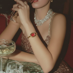 Woman in a sparkling dress with jewelry, holding a glass of wine in a dimly lit setting.